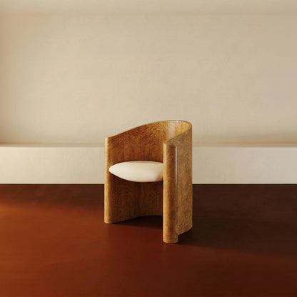 Golden wood Volute Chair by Garnier Pingree on a rust-coloured floor, with figured grain, scrolling sides and a cream seat.