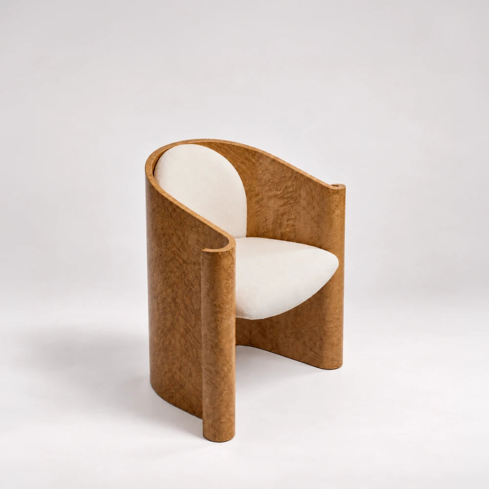 Elevated three-quarter view of the Volute Chair by Garnier Pingree, showing golden figured wood, rolled edges and cream seat and back cushions.