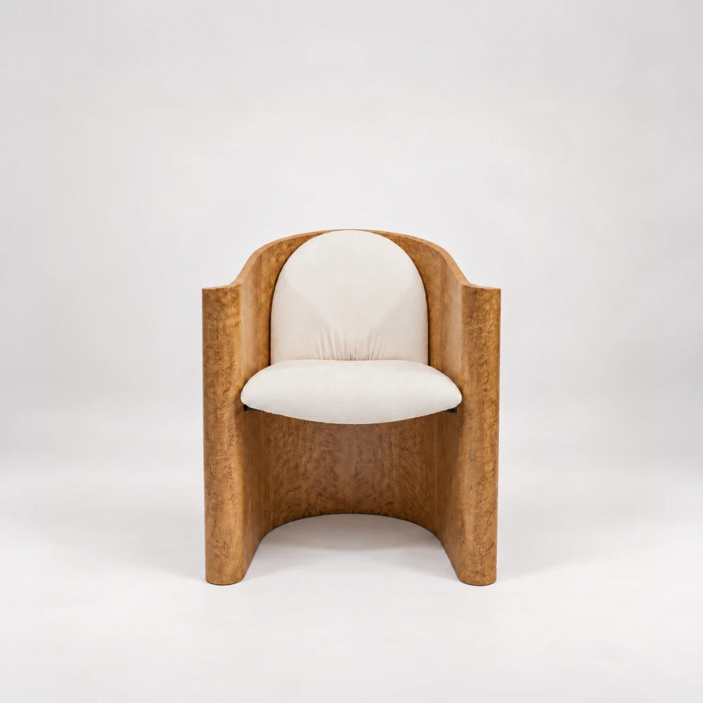 Front view of the Volute Chair by Garnier Pingree, with cream seat and rounded back cushions enclosed by a golden wood shell.