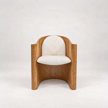 Front view of the Volute Chair by Garnier Pingree, with cream seat and rounded back cushions enclosed by a golden wood shell.