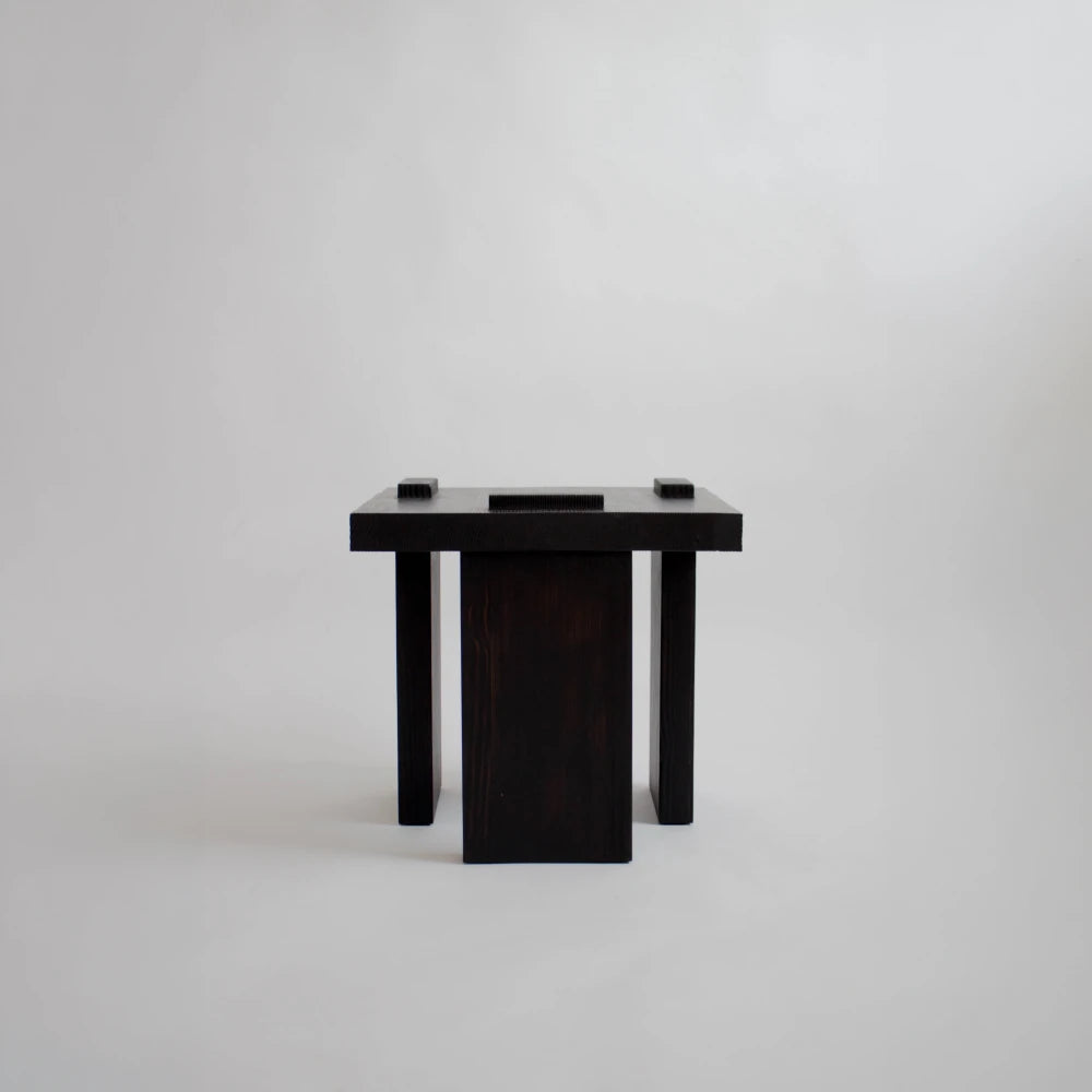 Front view of the Itooraba Stool Black by Sizar Alexis, featuring burned and stained pine with three asymmetric slab supports.