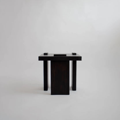 Front view of the Itooraba Stool Black by Sizar Alexis, featuring burned and stained pine with three asymmetric slab supports.