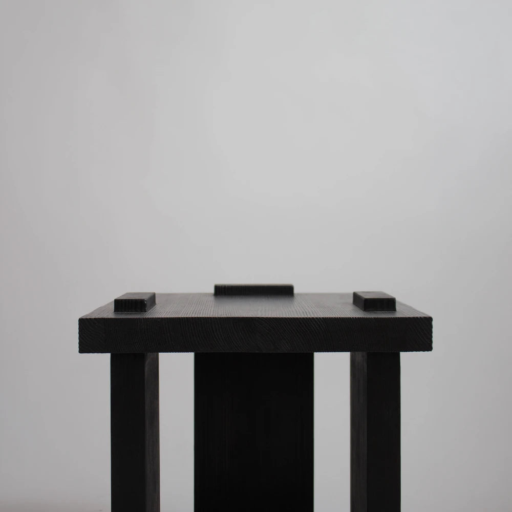 Detailed front view of the Itooraba Stool Black by Sizar Alexis, highlighting its thick square seat and raised wooden elements.