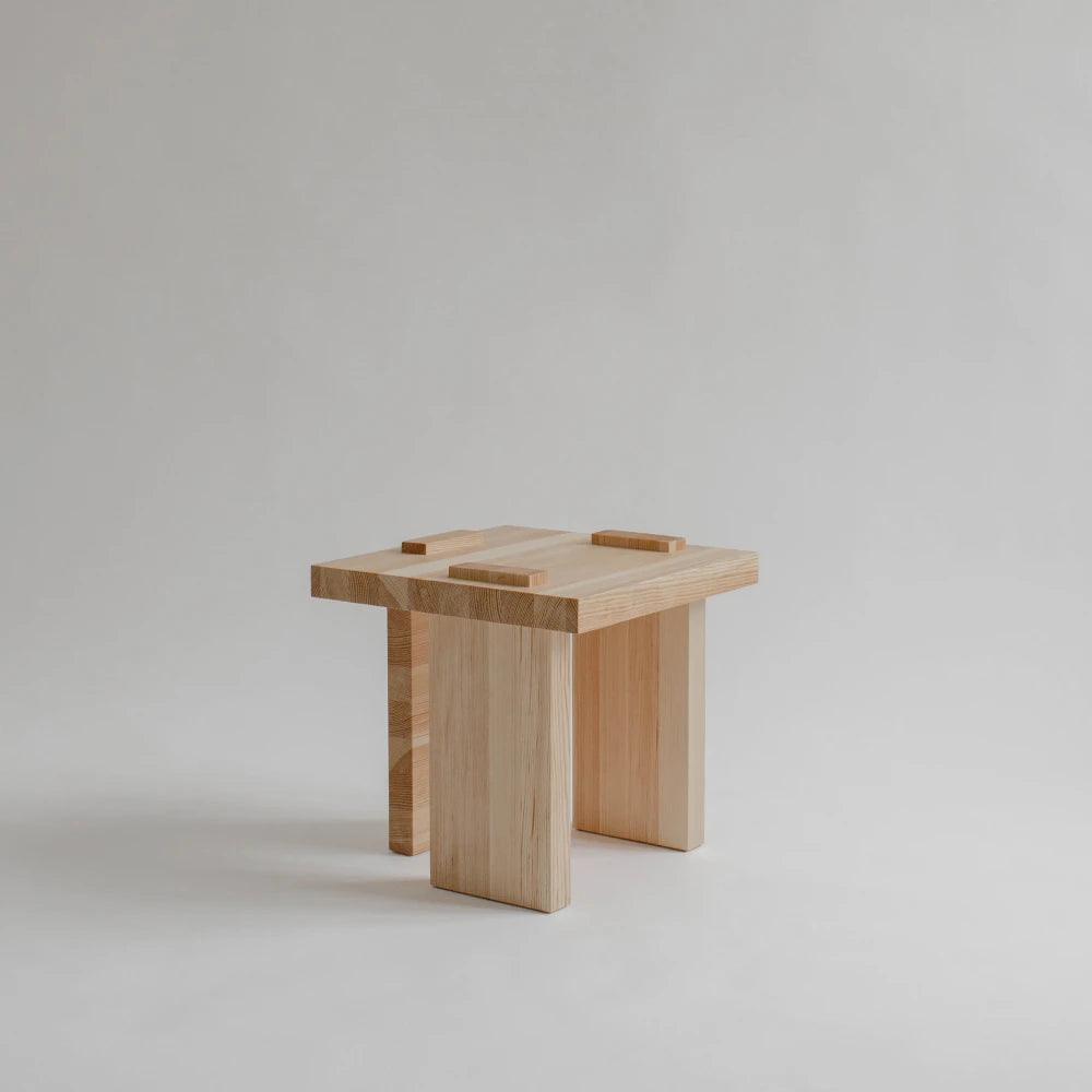 Three-quarter view of the Itooraba Stool by Sizar Alexis, featuring a square solid pine seat, geometric slab legs and raised tabletop details.