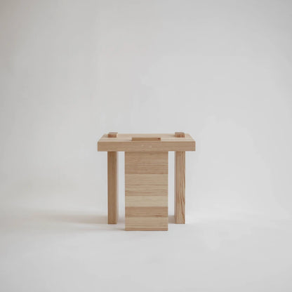 Side view of the Itooraba Stool by Sizar Alexis, highlighting its asymmetric solid pine supports and visible wooden joinery.