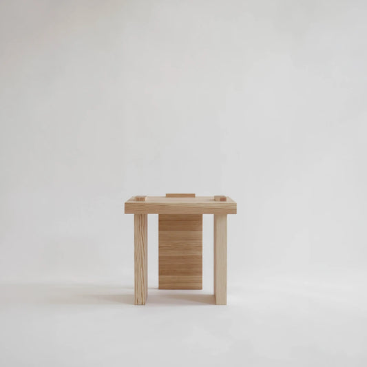 Front view of the Itooraba Stool by Sizar Alexis, showing its square seat, three pine supports and architectural construction.