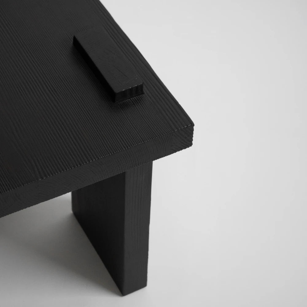 Close-up of the Itooraba Stool Black by Sizar Alexis, revealing the burned pine grain, raised tabletop detail and slab leg.