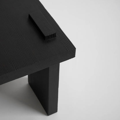 Close-up of the Itooraba Stool Black by Sizar Alexis, revealing the burned pine grain, raised tabletop detail and slab leg.