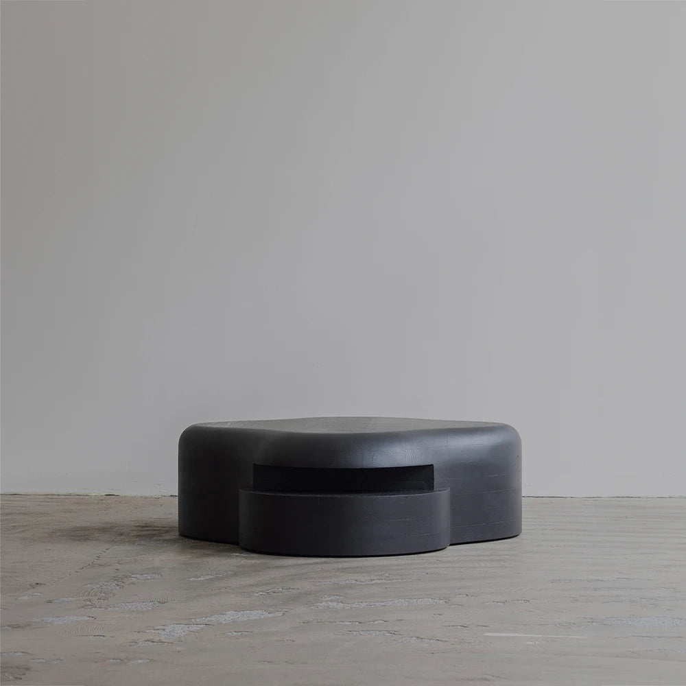 Low frontal view of the Lahmu Coffee Table by Sizar Alexis, defined by a monolithic black form and projecting circular element.