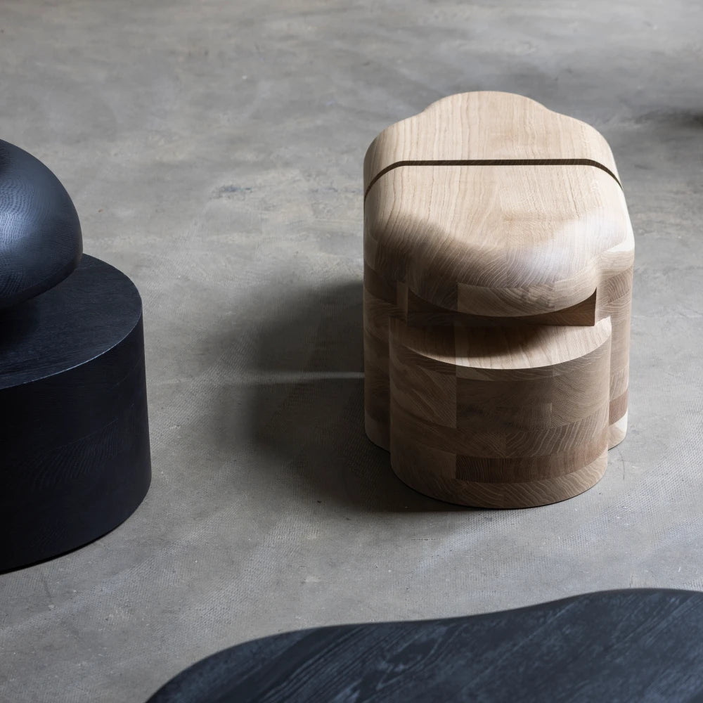 Lahmu Stool Natural by Sizar Alexis shown from above in a studio setting, with rounded oak forms and contrasting dark furniture.
