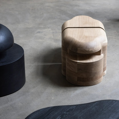 Lahmu Stool Natural by Sizar Alexis shown from above in a studio setting, with rounded oak forms and contrasting dark furniture.