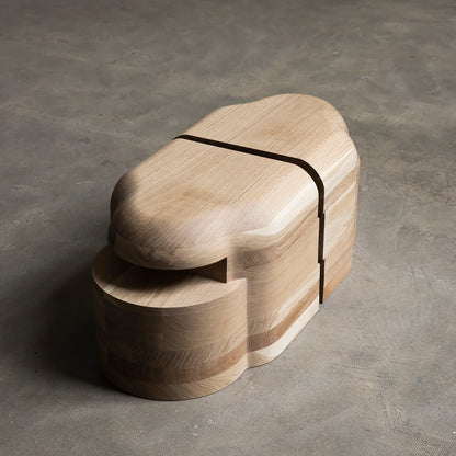 Lahmu Stool Natural by Sizar Alexis in a high three-quarter view, showcasing smooth oak curves, visible grain, and dark inset line.
