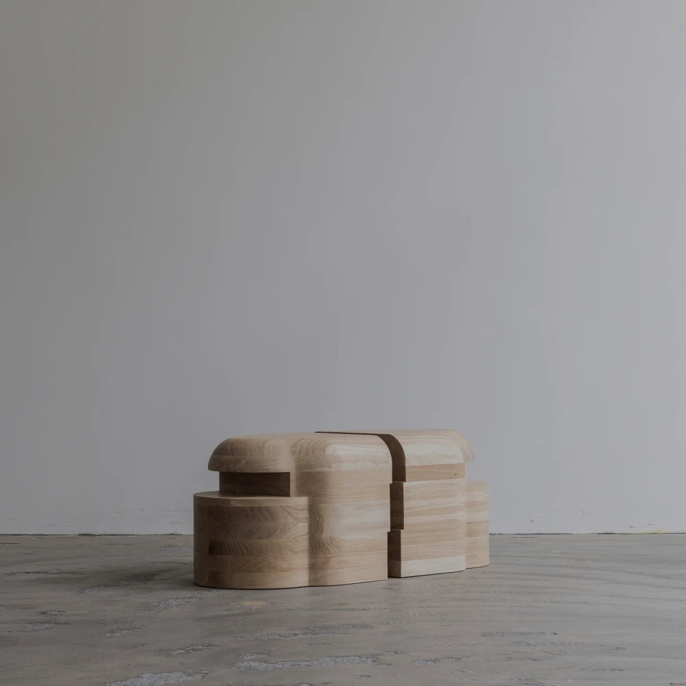 Side view of the Lahmu Stool Natural by Sizar Alexis against a minimal studio wall, emphasizing its compact, interlocking silhouette.