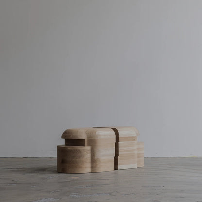 Side view of the Lahmu Stool Natural by Sizar Alexis against a minimal studio wall, emphasizing its compact, interlocking silhouette.