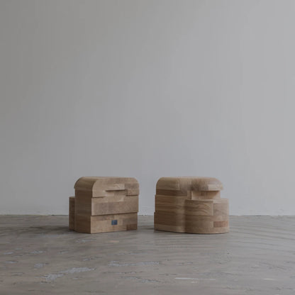 Two Lahmu Stool Natural pieces by Sizar Alexis viewed from opposite sides, displaying layered oak construction and distinctive geometric recesses.