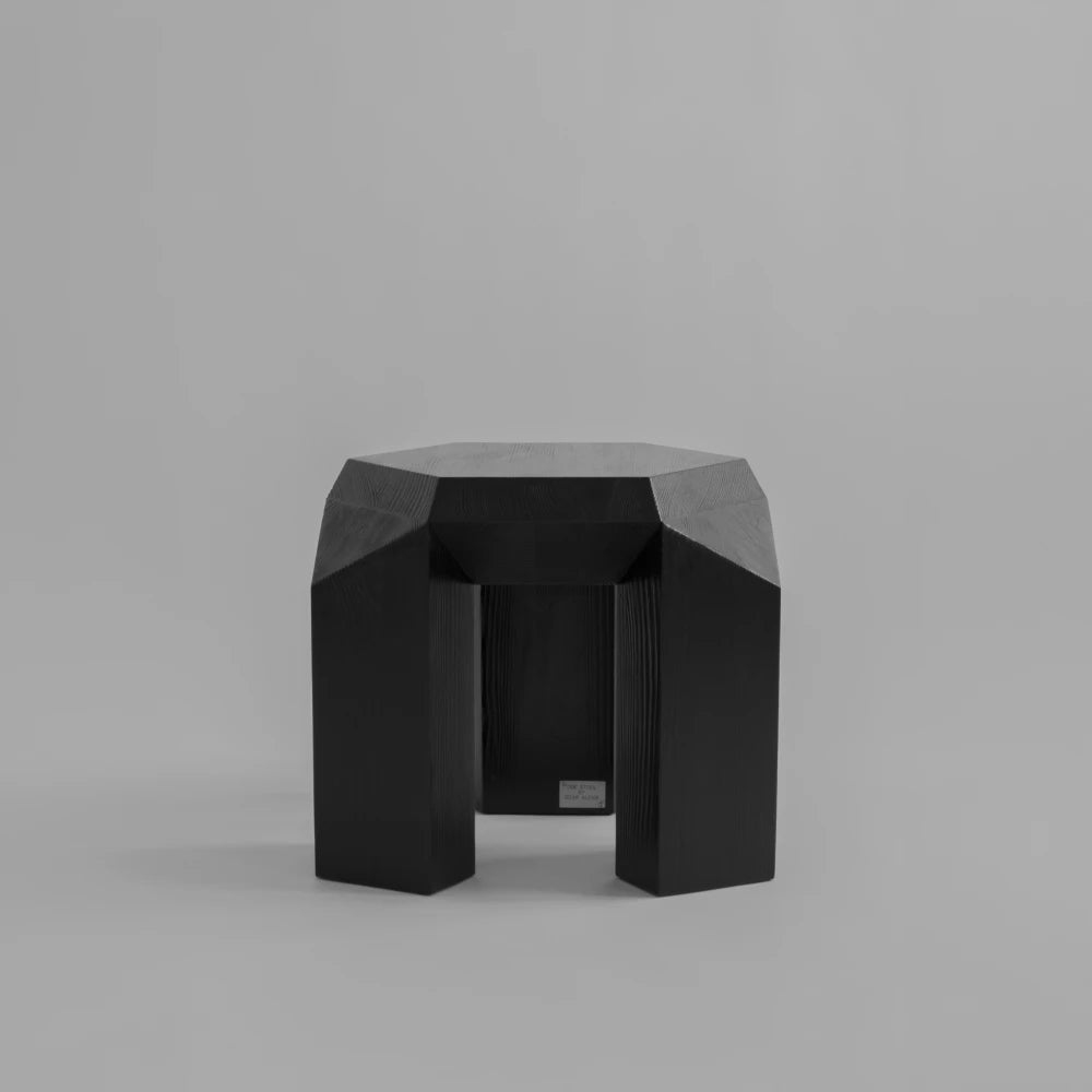 Closer front view of the black Ode Three-Legged Stool by Sizar Alexis, highlighting its substantial legs, angular joinery, and wood grain.