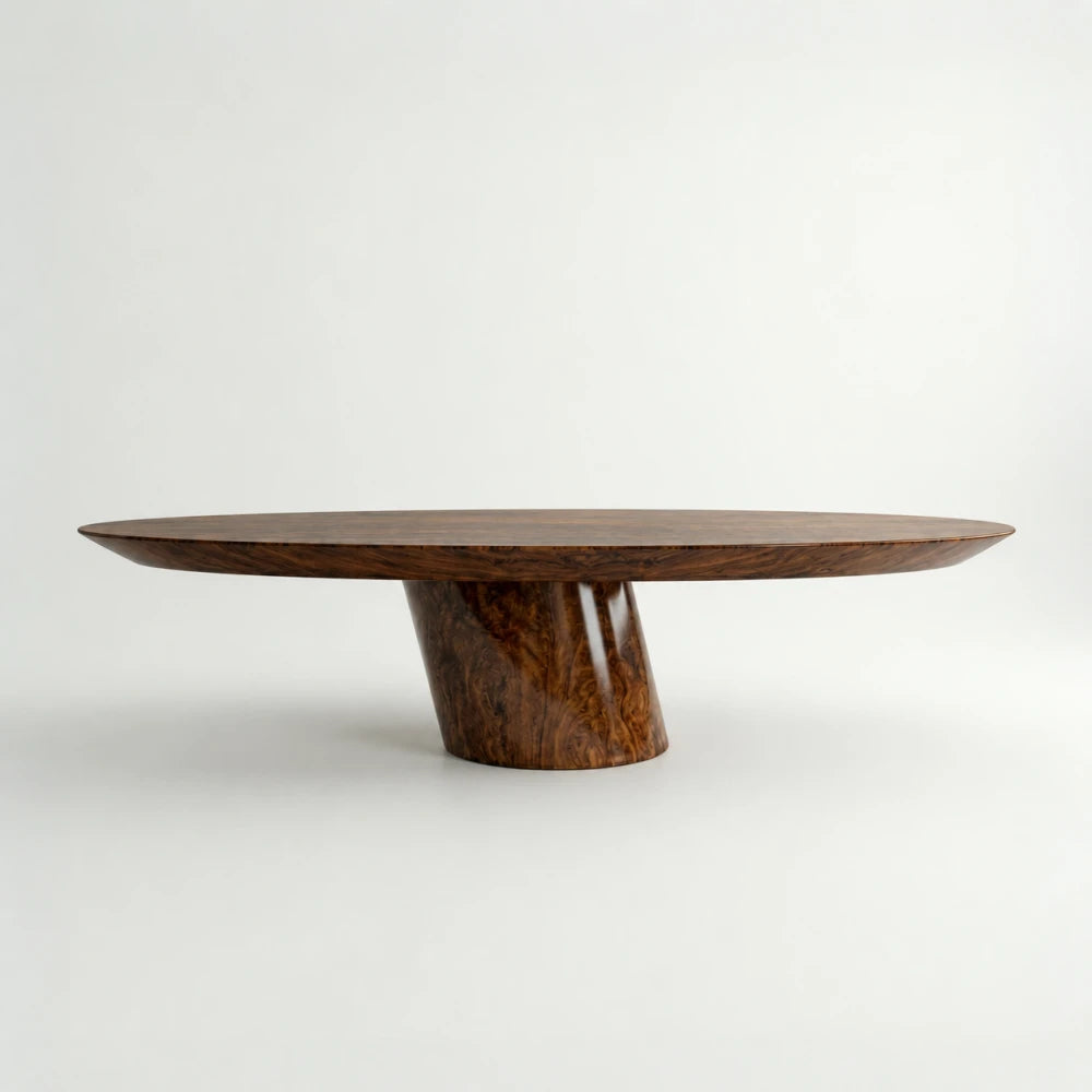 Side profile of the Deus Burl Dining Table by Studio Romell, showing its long oval top balanced on an inclined walnut burl pedestal. STUDIO ROMELL