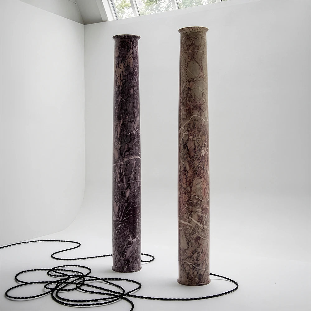 Three-quarter studio view of two Eldpelare Marble Lamps by Studio Romell, accompanied by long black braided cords arranged across the floor.
