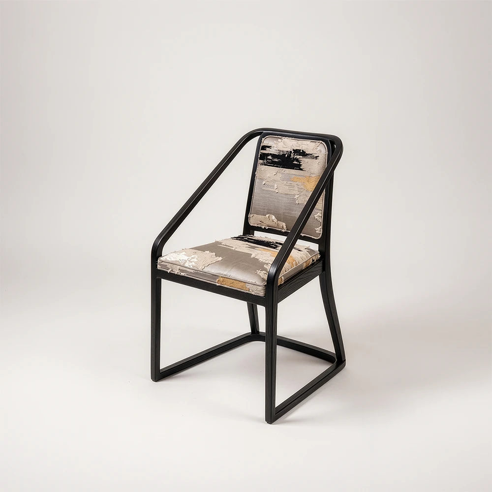 Oblation Dining Chair by Studio Romell, featuring a black wooden frame, sloping armrests and textured upholstery in grey, cream, black and ochre.