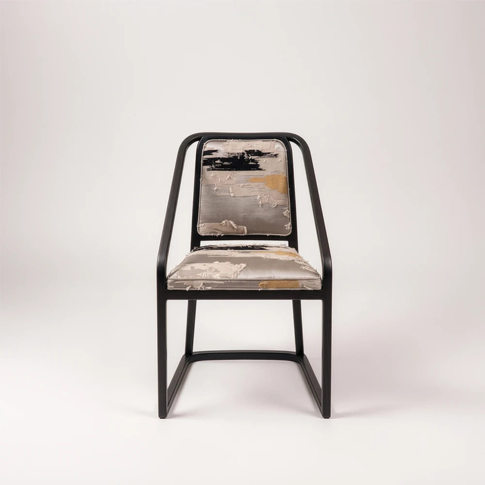 Front view of the Oblation Dining Chair by Studio Romell, highlighting its angular black wooden frame and abstract patterned seat and back cushions.