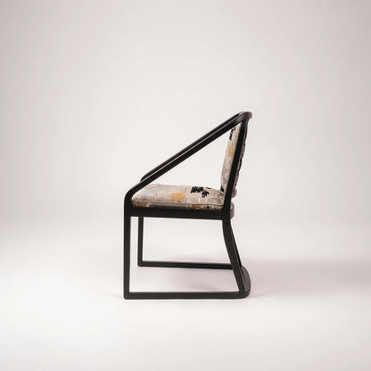 Side profile of the Oblation Dining Chair by Studio Romell, showing long sloping armrests, a curved rear frame and a continuous sled base.