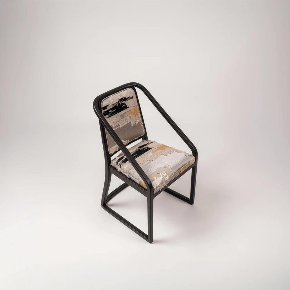 Elevated three-quarter view of the Oblation Dining Chair by Studio Romell, revealing its patterned upholstery, open sides and sculptural black wooden frame.
