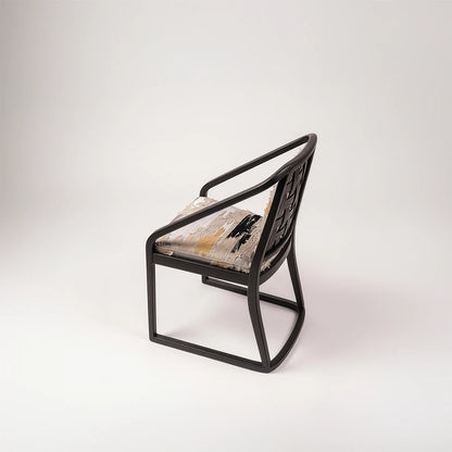Angled side view of the Oblation Dining Chair by Studio Romell, showing its interwoven wooden backrest, sweeping armrests and grey upholstery with contrasting motifs.