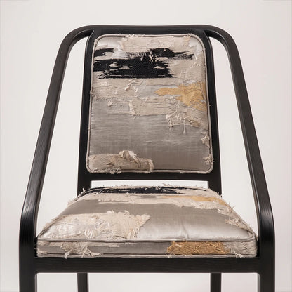 Close-up of the Oblation Dining Chair by Studio Romell, highlighting raised, frayed textile patterns in cream, black and ochre across the seat and backrest.