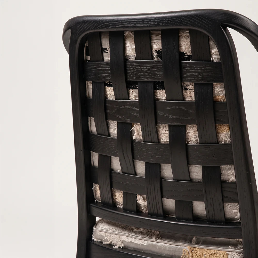 Rear detail of the Oblation Dining Chair by Studio Romell, featuring interwoven black wooden slats with visible grain and patterned upholstery beneath.