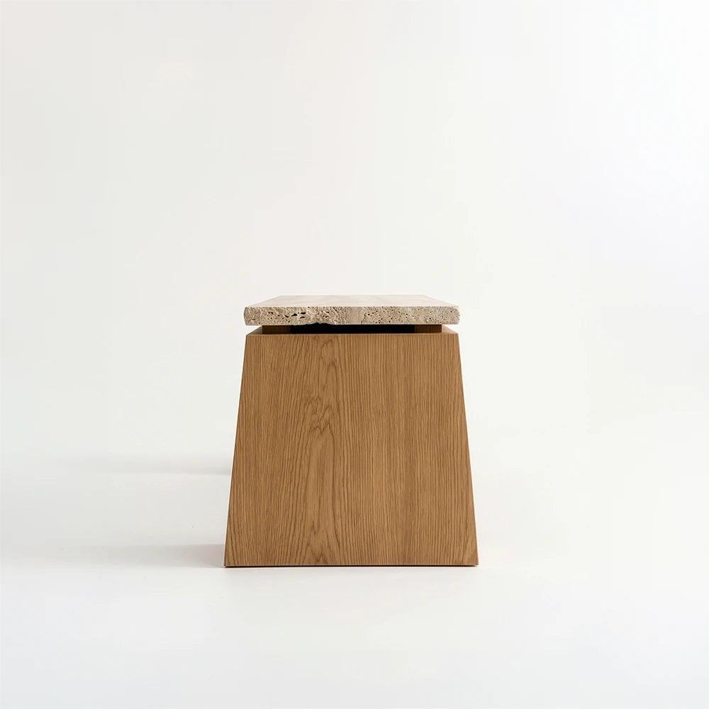 Side view of the Santos Desk by Studio Romell, highlighting a tapered wooden support with visible grain beneath a pale stone slab with a rough edge.