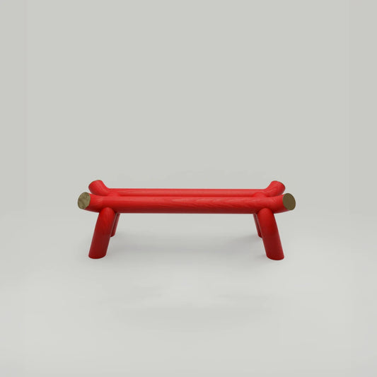 Vista frontal del banco Torii Bench rojo, de Ultramar Studio, sobre un fondo claro, que destaca su asiento alargado, sus largueros elevados y sus patas abiertas.