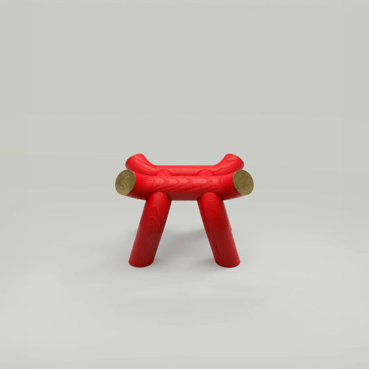 Vista frontal del taburete Torii Stool rojo, de Ultramar Studio, sobre un fondo claro, que muestra los largueros elevados del asiento, las patas abiertas y los remates dorados.